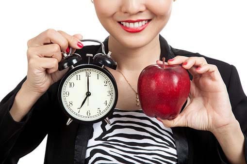 young smiling woman holding an alarm clock in one hand and an apple in another