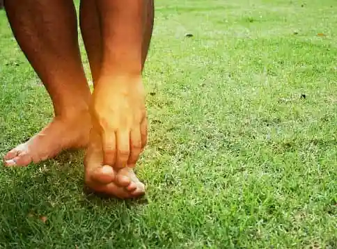 man scratching his foot in grass