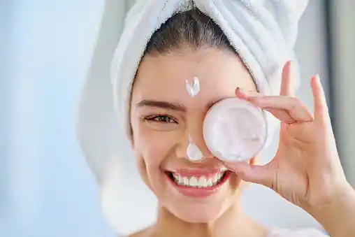 happy young woman applying moisturizer to her skin after bath