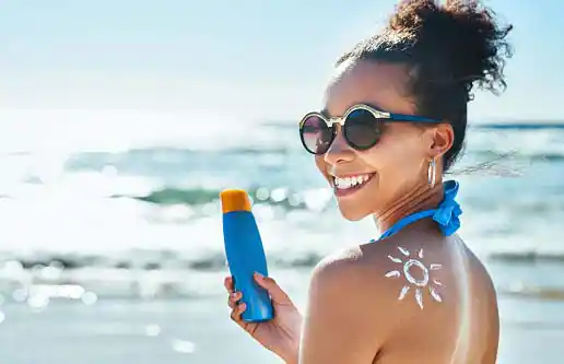 happy young woman using sunscreen bottle in sun by sea-side